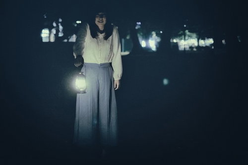 暗闇の中でランタンを手にした謎の女性、白い服で夜間に立つ不気味な姿