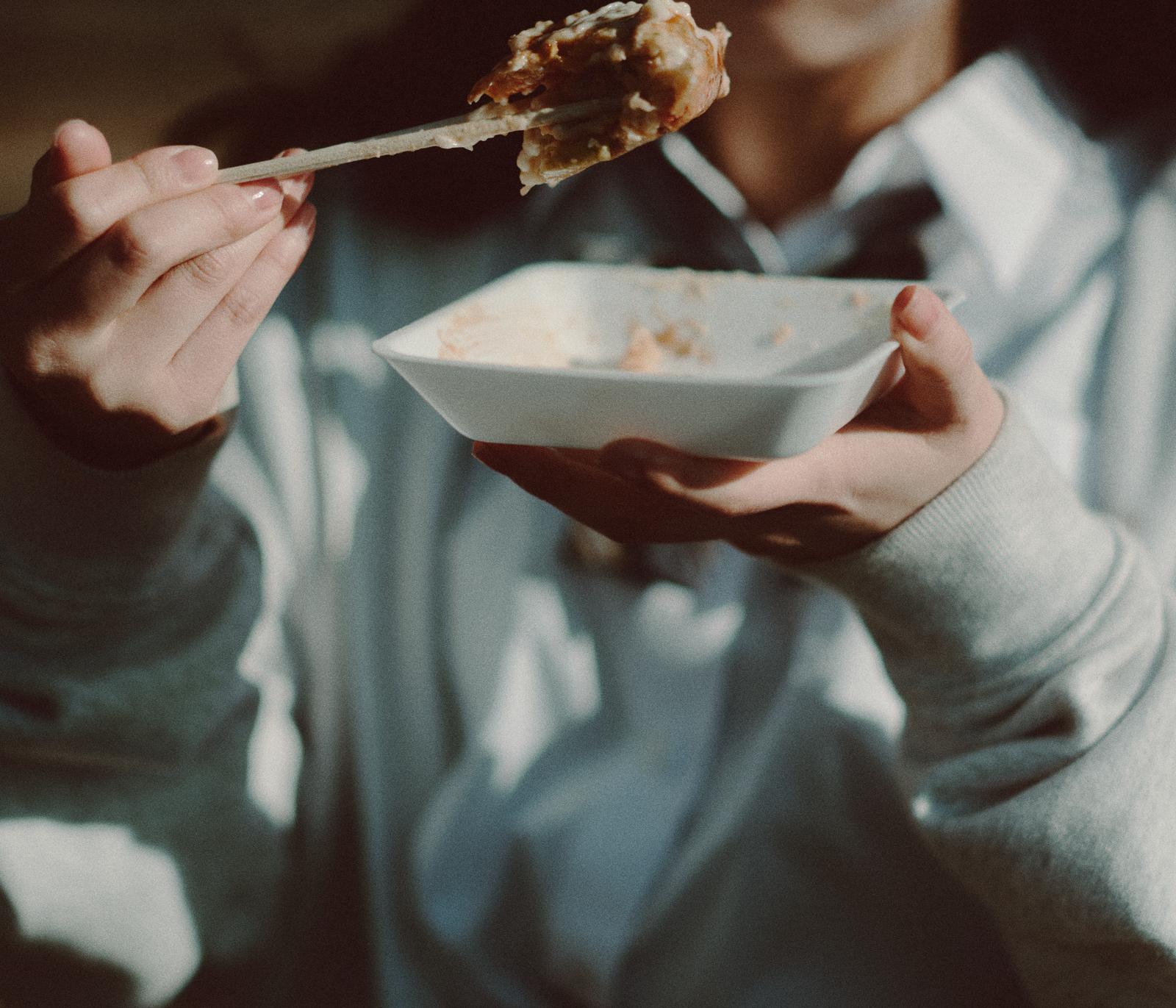 マヨネーズがついたたこ焼きを割り箸で食べ歩く女子高生