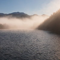 朝靄に包まれたため池の水面に立つさざ波と逆光の写真
