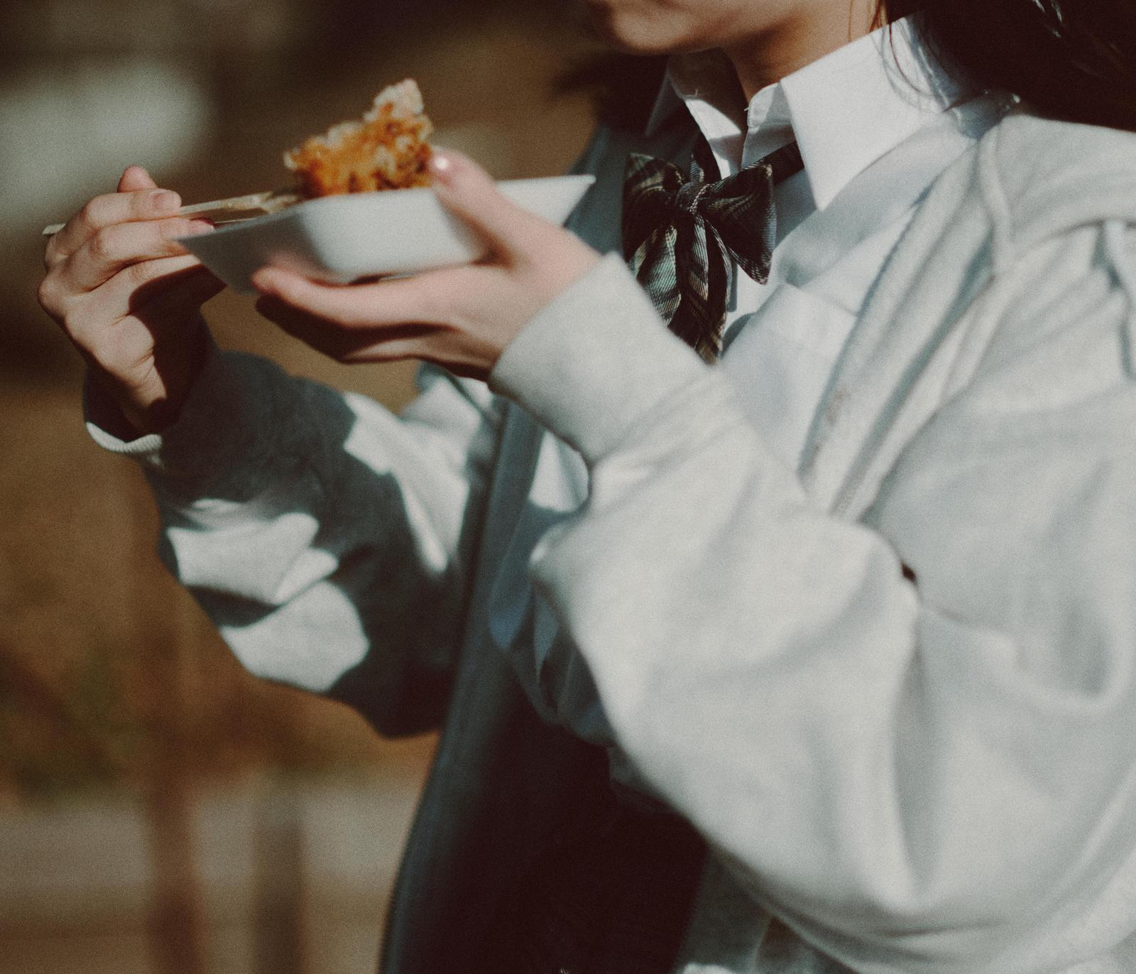 白い小皿で揚げ物を食べる制服姿の女子高生