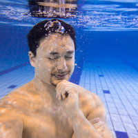 屋内プールの水中で瞑想する男性の写真