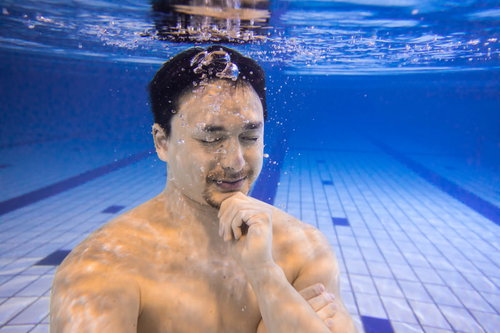 屋内プールの水中で瞑想する男性