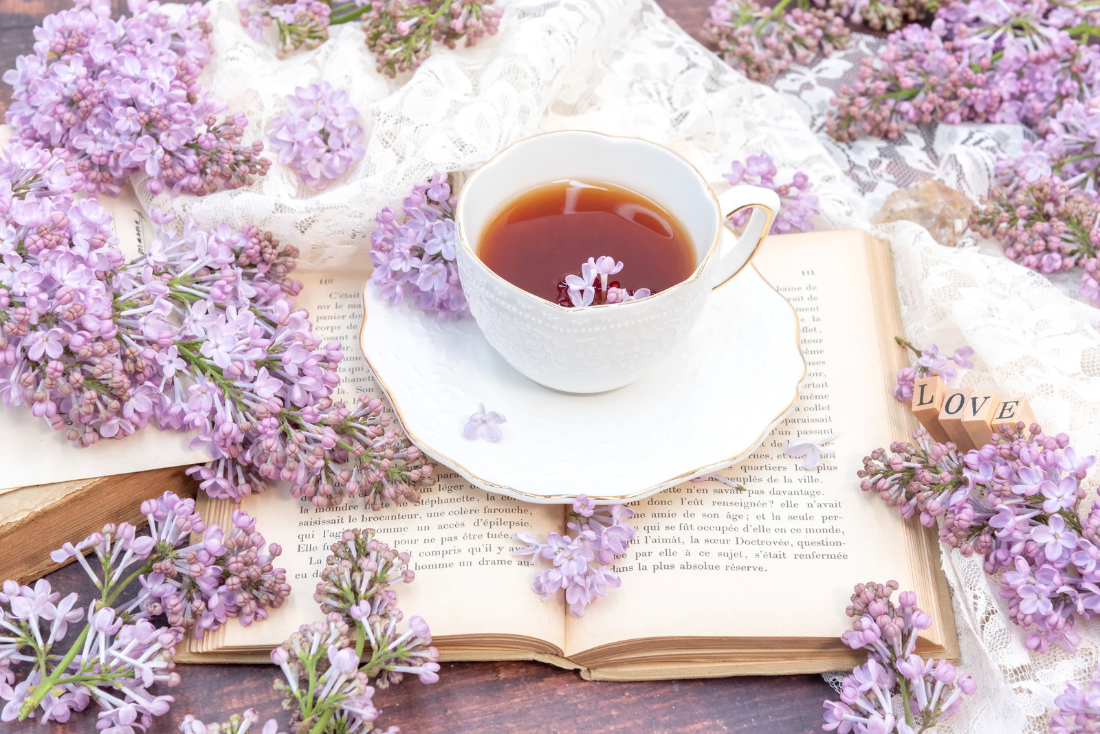 白いティーカップに入った紅茶と紫色のライラックの花、洋書