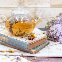 洋書の上に置かれたティーポットとライラックの花の写真