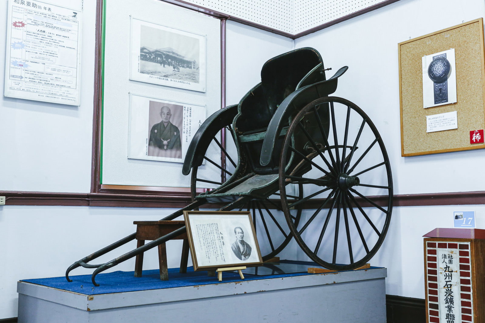 博物館の展示室に展示された古い黒い人力車と大きな車輪