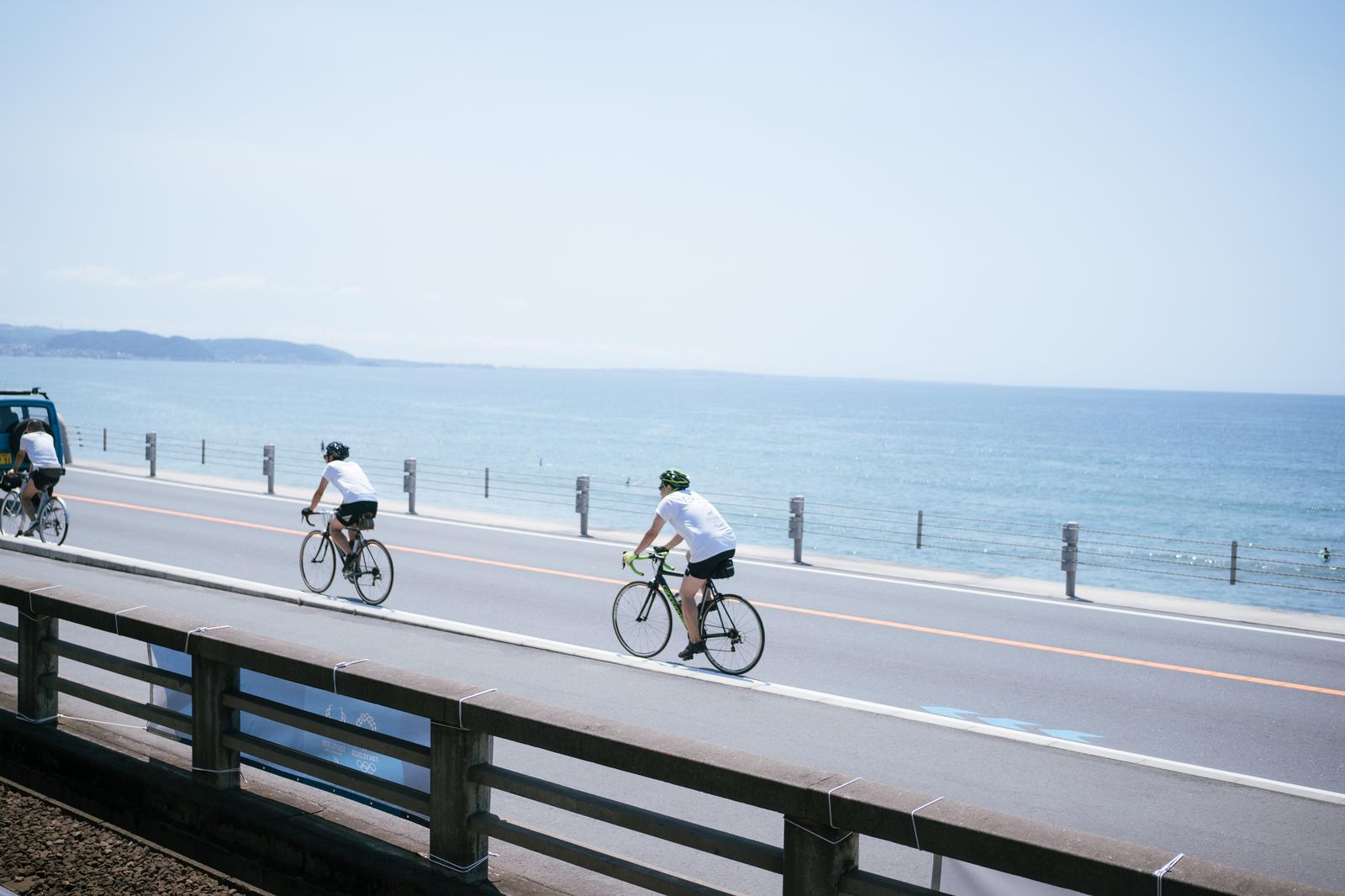 海岸沿いの車道をロードバイクで走る複数のサイクリスト