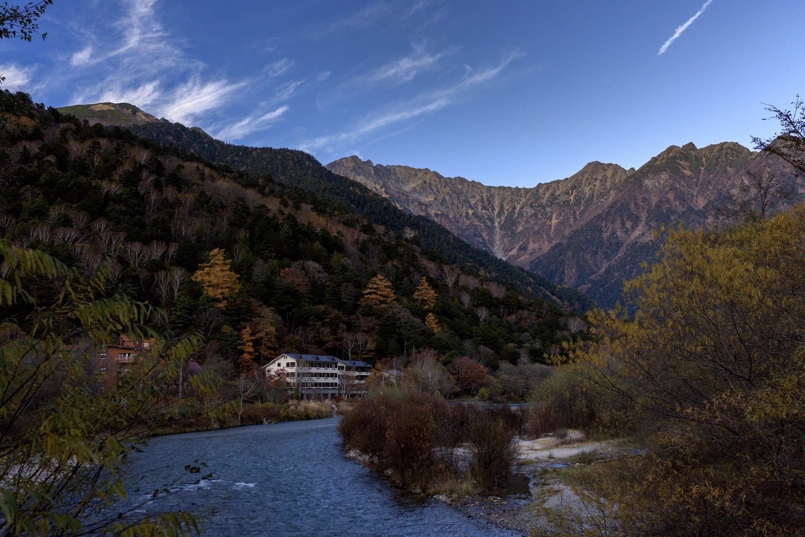 秋の上高地で焼岳を背景に紅葉した木々と清流が流れる山岳風景