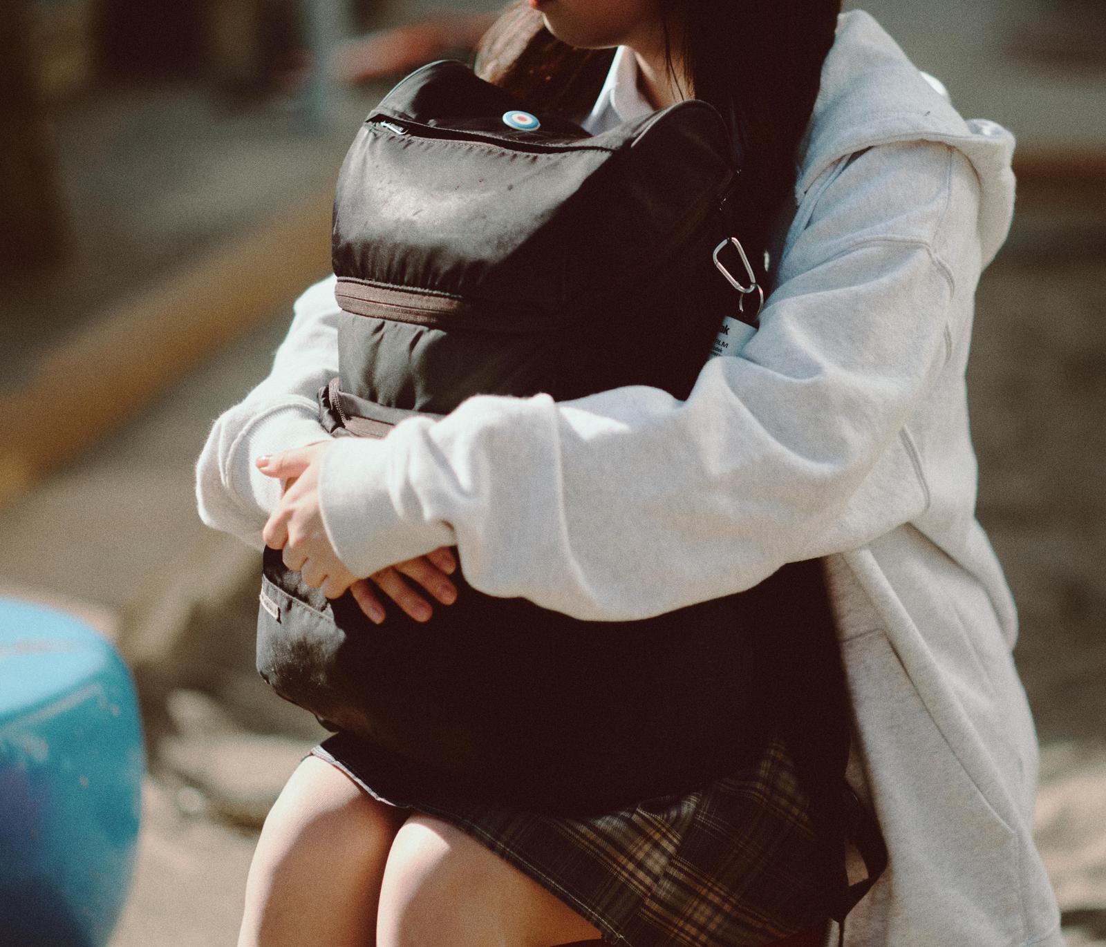 黒いリュックを抱えて座る白いパーカーを着た女性