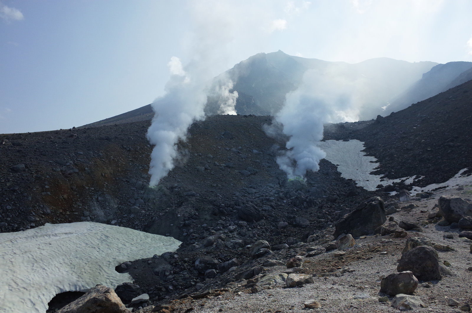 火口から白い噴煙を上げる旭岳の山頂付近の風景