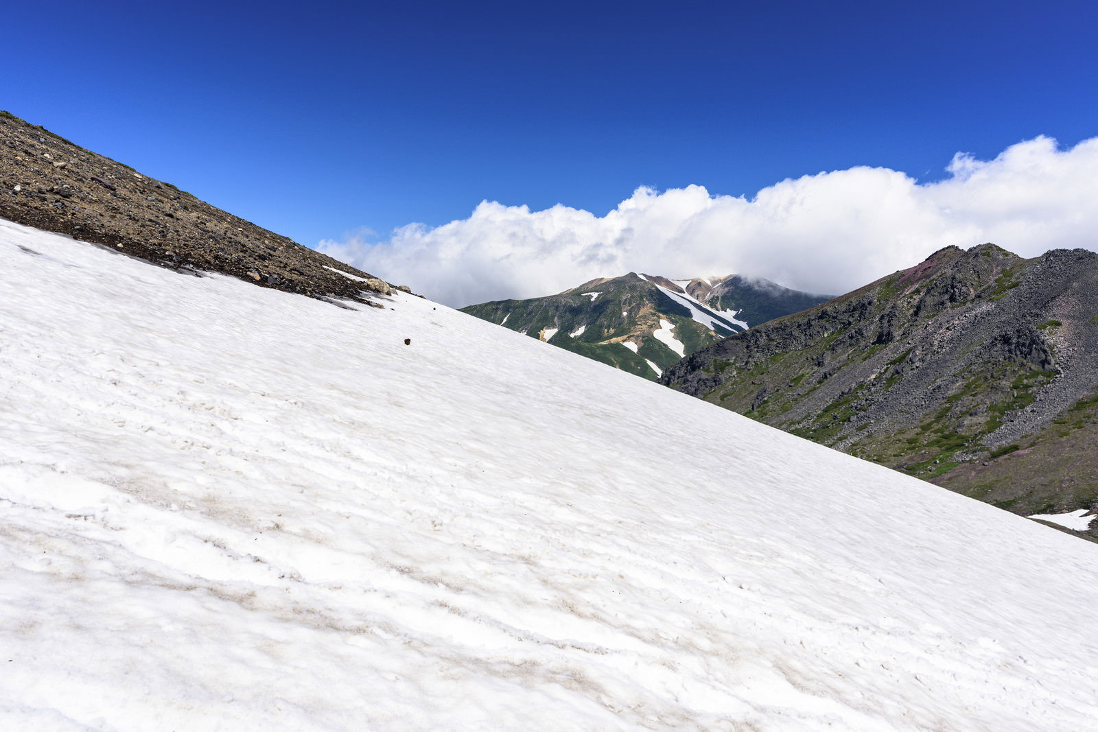 青空の下、夏でも雪渓が残る旭岳の山肌と白い雪面