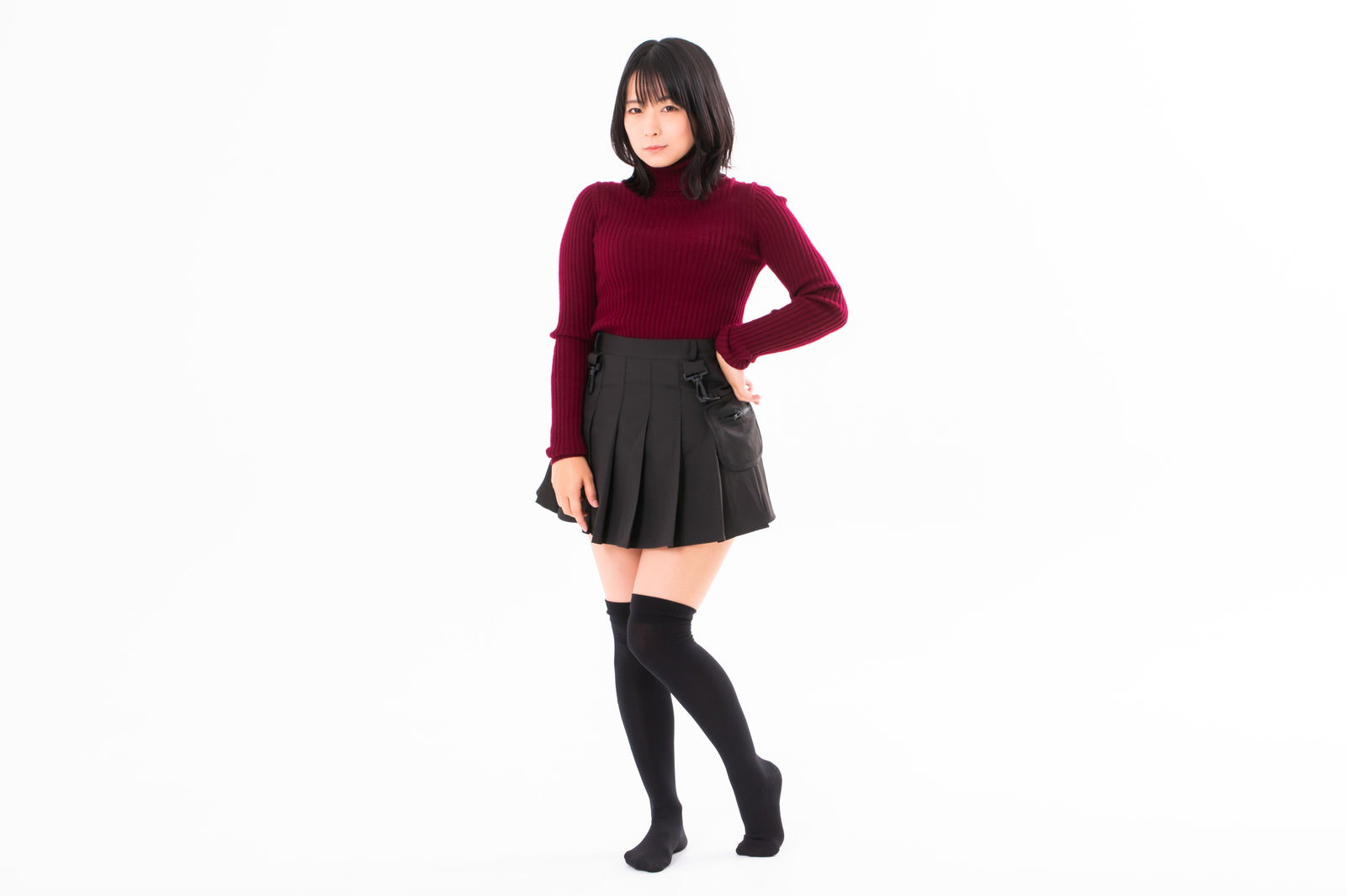 白背景で腰に手を当てポージングする赤いトップスの女性［モデル：にゃるる］