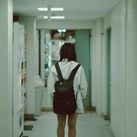 廊下を歩く制服姿の女子高生の後ろ姿、リュックを背負った学生の写真