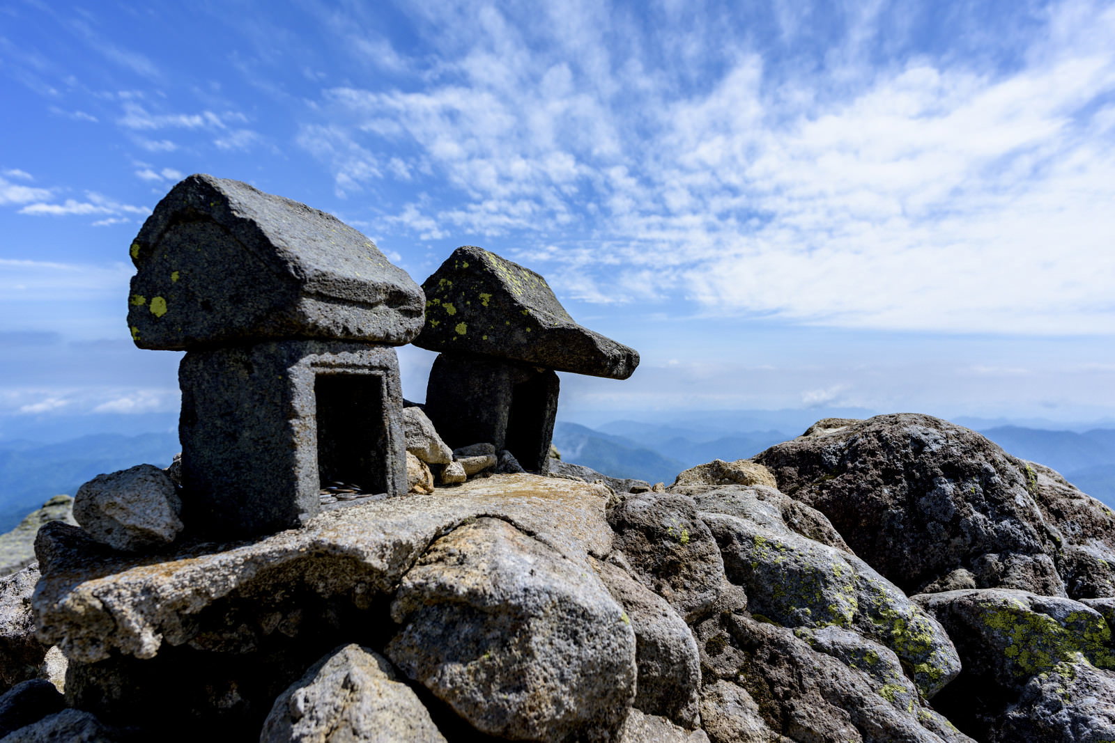 燧ヶ岳山頂の岩場に建つ石造りの祠と青空に浮かぶ白い雲
