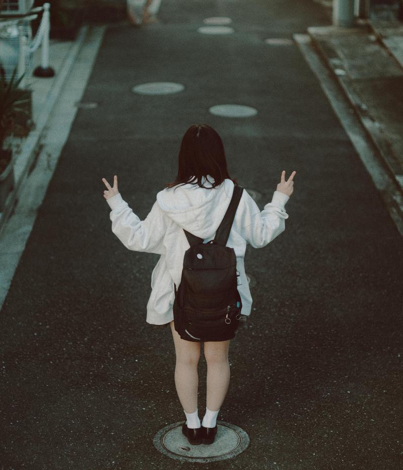 路上で両手でピースをする後ろ姿の制服姿の女子高生