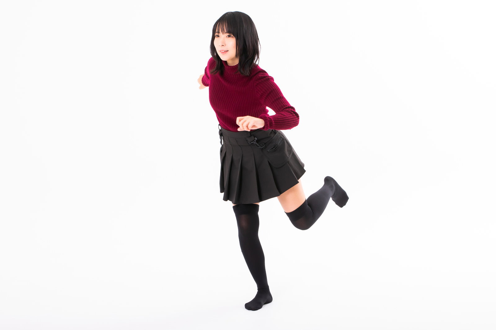 赤いセーターと黒いスカートを着て片足を上げて小走りする女性［モデル：にゃるる］