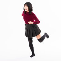 赤いセーターと黒いスカートで片足を上げてダッシュで駆け出す女性の写真