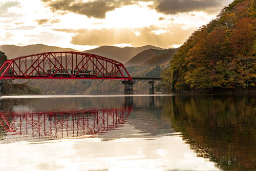 水面に映り込む赤い鉄橋と電車車両（JR北上線）
