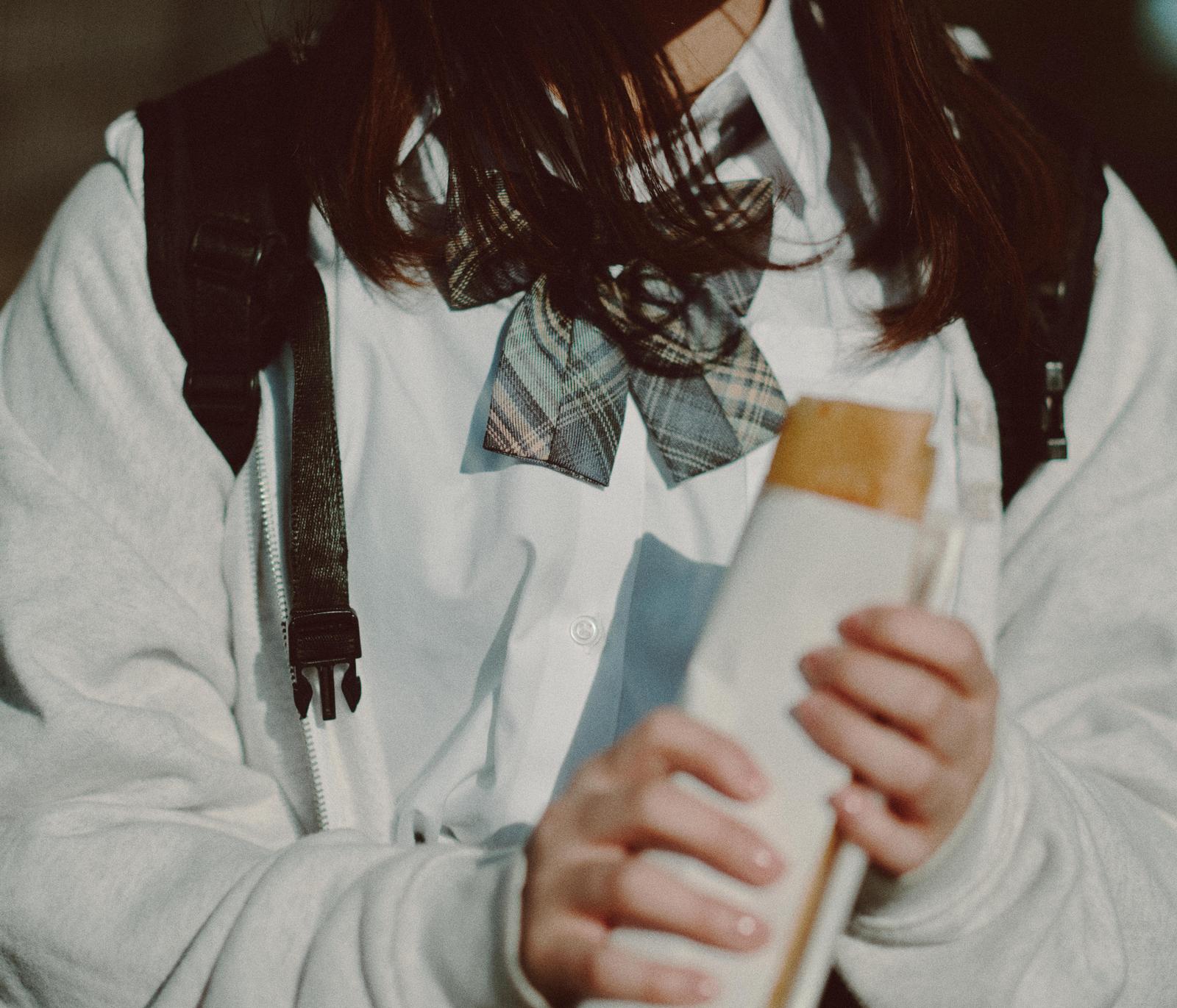チェック柄リボン付きの制服を着て、食べ物の袋を持つ女性