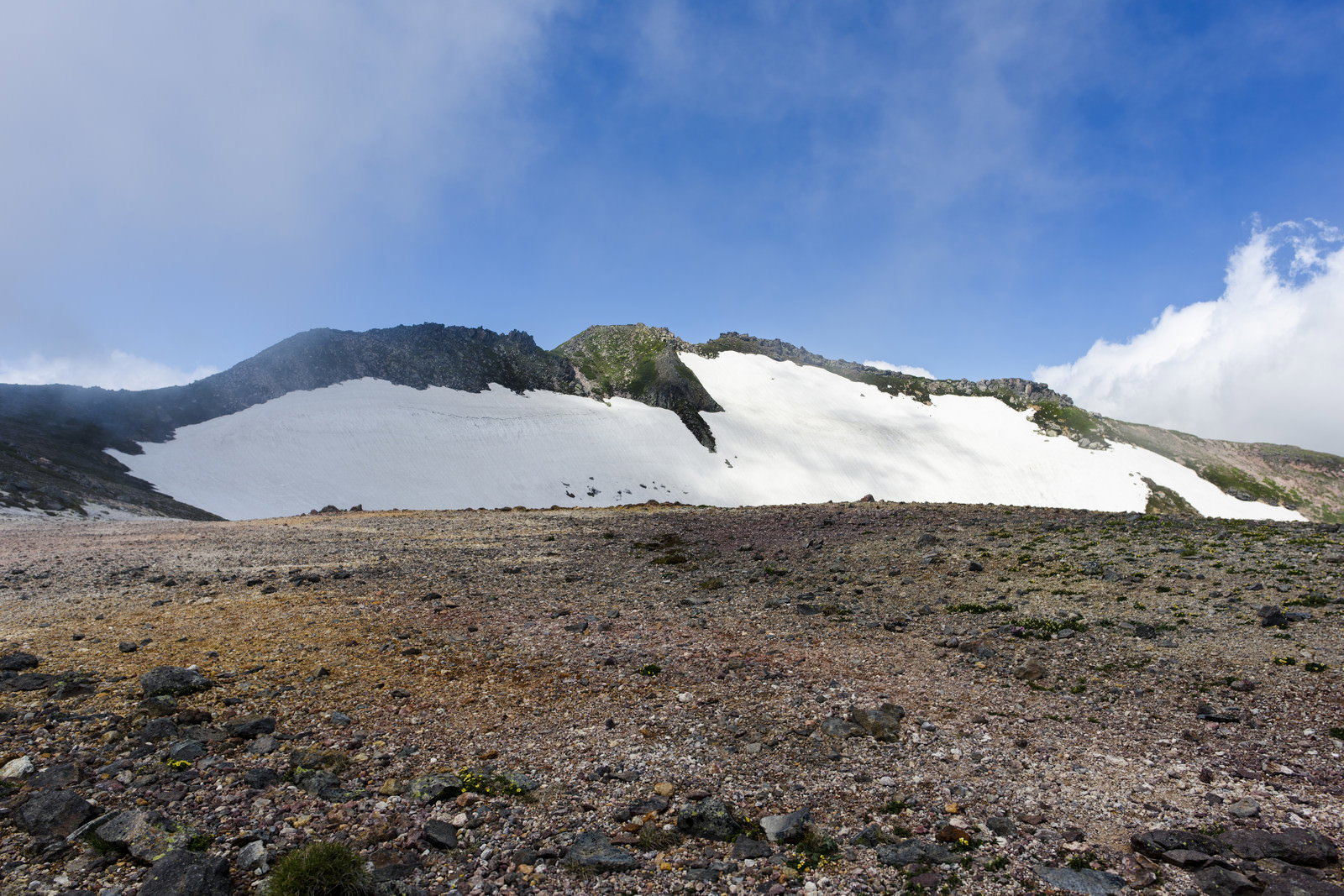 残雪に覆われた大雪山の山肌と青空に浮かぶ白い雲の風景