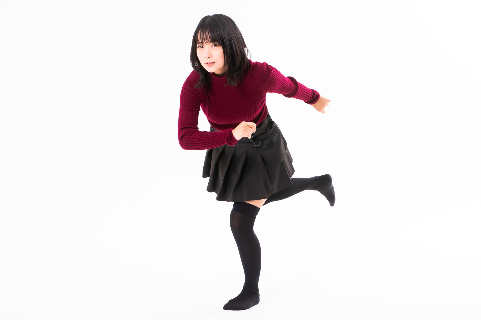 赤いニットを着た女性が片足を上げて駆け出すポーズをしている［モデル：にゃるる］
