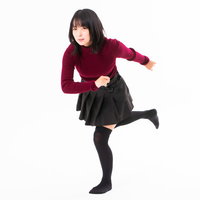 赤いニットを着て片足を上げて駆け出す女性の写真