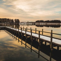 夕焼けに染まる湖面と木製桟橋のリフレクションの写真