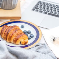 クロワッサンとティーカップが置かれたデスク周りの作業風景の写真