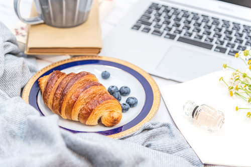 クロワッサンとティーカップが置かれたデスク周りの作業風景