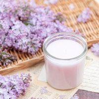 竹製マットの上に並ぶ白いキャンドルと淡紫色のライラックの写真