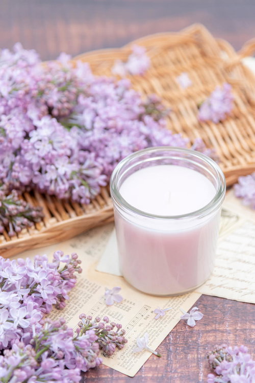 竹製マットの上に並ぶ白いキャンドルと淡紫色のライラック