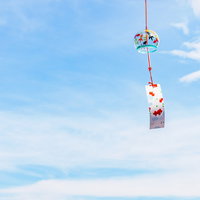 赤い紐の風鈴が風で揺れる夏の日中、青空の下で涼しげに音色を響かせるの写真