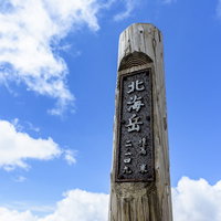 青空に聳え立つ大雪山北海岳の木碑と山頂の景観の写真