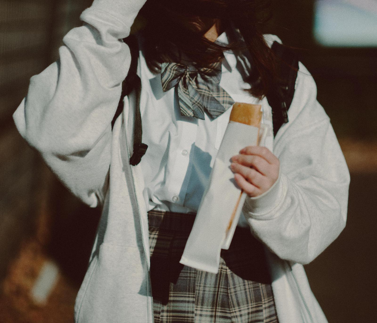 制服を着た女子高生が紙袋を持って買い食いをしている様子