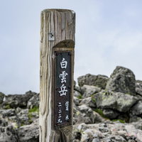 背景に雲が広がる大雪山白雲岳の木碑と山頂景観の写真