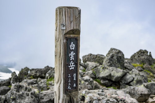 背景に雲が広がる大雪山白雲岳の木碑と山頂景観