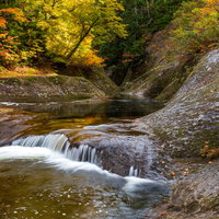 秋の小又峡を流れる紅葉に囲まれた清流と岩場の渓流風景の写真