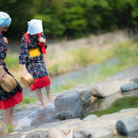 赤い腰巻きと黄色い帯をつけた姉さんが川辺でフミフミ洗濯（足踏み洗濯）の写真