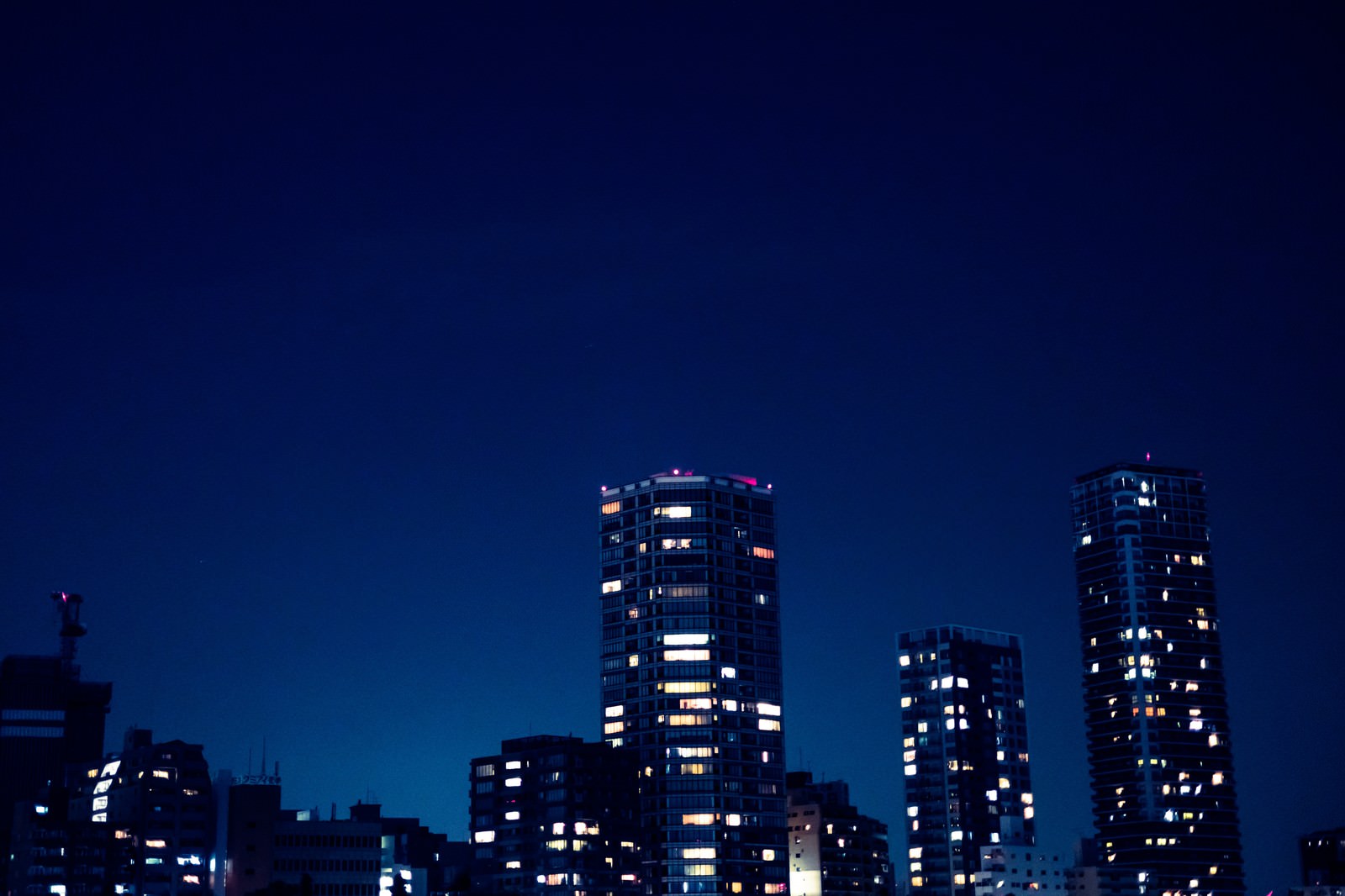 深い青色の夜空を背景に立ち並ぶ複数の高層ビル群