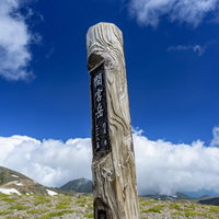 青空と雲を背景に中央に立つ大雪山間宮岳の木碑の写真