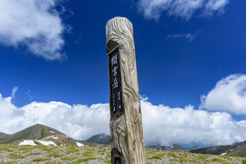 青空と雲を背景に中央に立つ大雪山間宮岳の木碑