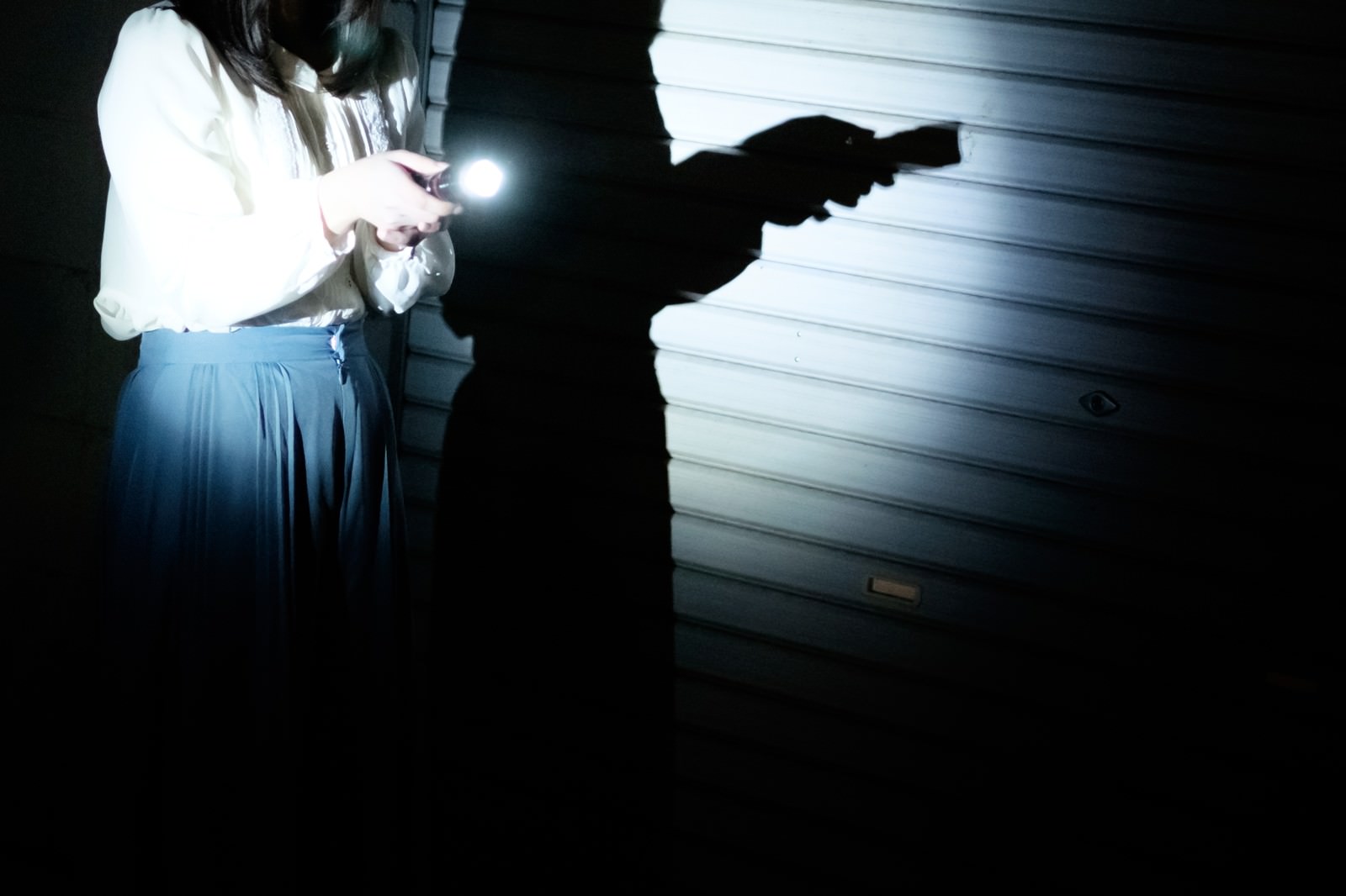 懐中電灯の光で照らされた暗闇の中を歩く女性のシルエット［モデル：さとうゆい］