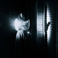 懐中電灯を持って暗闇を恐る恐る歩く女性の写真