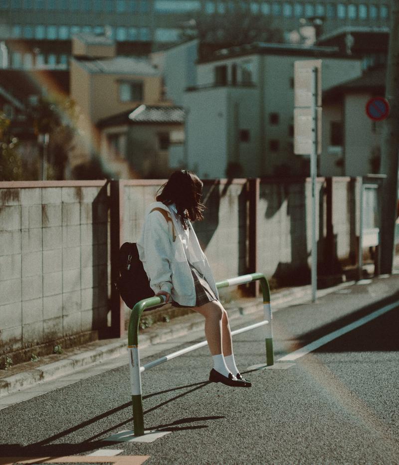 通学路の柵に腰掛ける女子高生