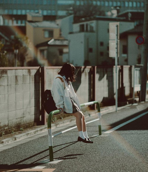 女子高生が通学路の柵に腰掛けている姿