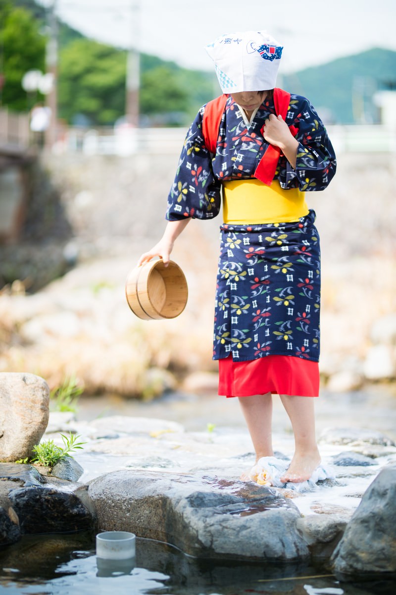 A woman in a kimono trampling laundry in a tub with her feet by the riverside
