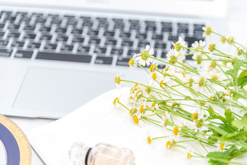 黄色い小花とMacbookが並ぶ清潔感のあるデスク