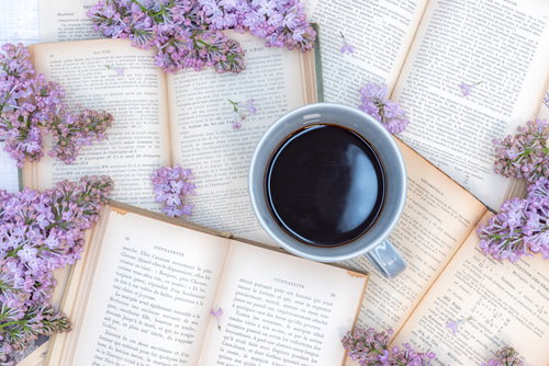 洋書に囲まれたコーヒーカップと紫のライラック