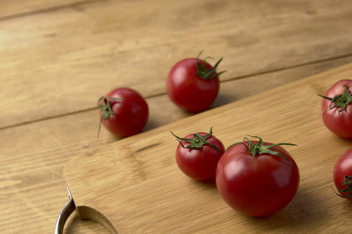 木製まな板の上に並ぶ赤いミニトマトと緑のヘタの写真
