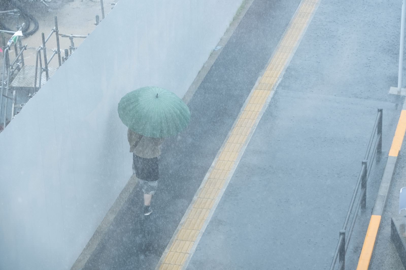 緑色の傘を差して土砂降りの雨の中を歩く女性