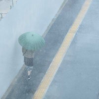 緑色の傘を差して土砂降りの中を帰宅する女性の写真